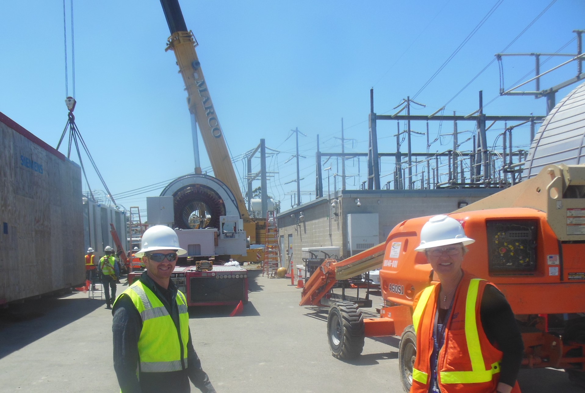 Project specialist T.J. Gates and project manager Irina Petersen standing in front of a synchronous condenser unit at the San Luis Rey substation.
